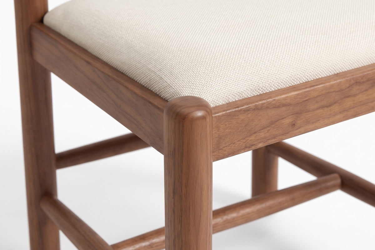 Albi Walnut Dining Chair: close-up of the ivory linen seat's edge set into the walnut seat frame, with a round stretcher below