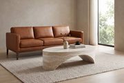 Alma oval sculpted coffee table in a cream travertine-look finish in a calm, daylit living room