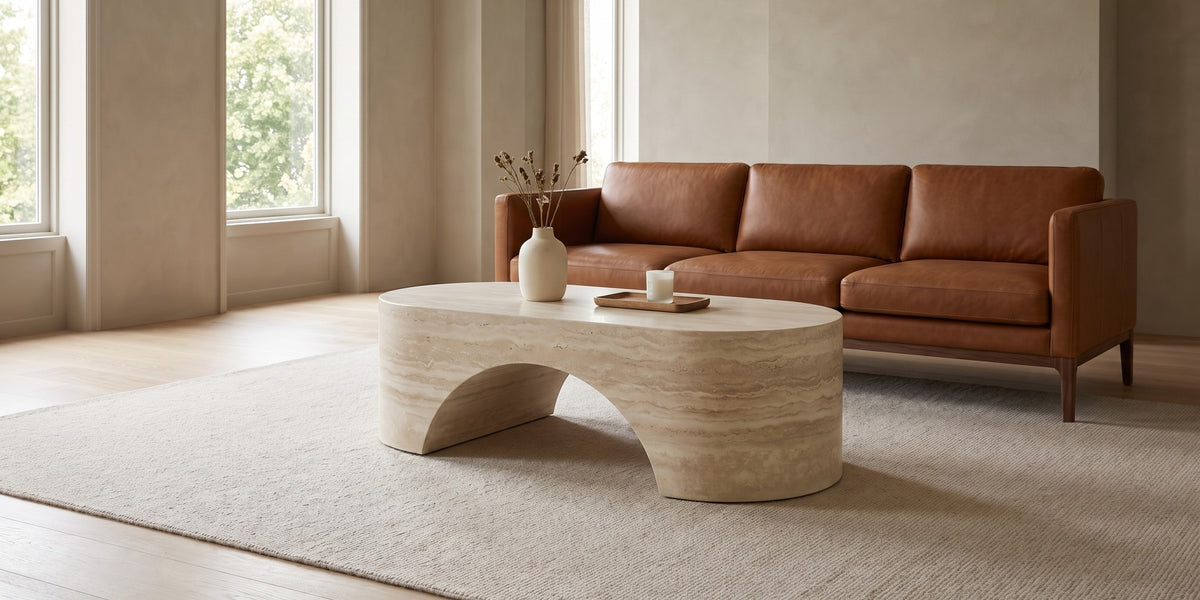 Alma oval sculpted coffee table in a cream travertine-look finish in a wide, calm living room