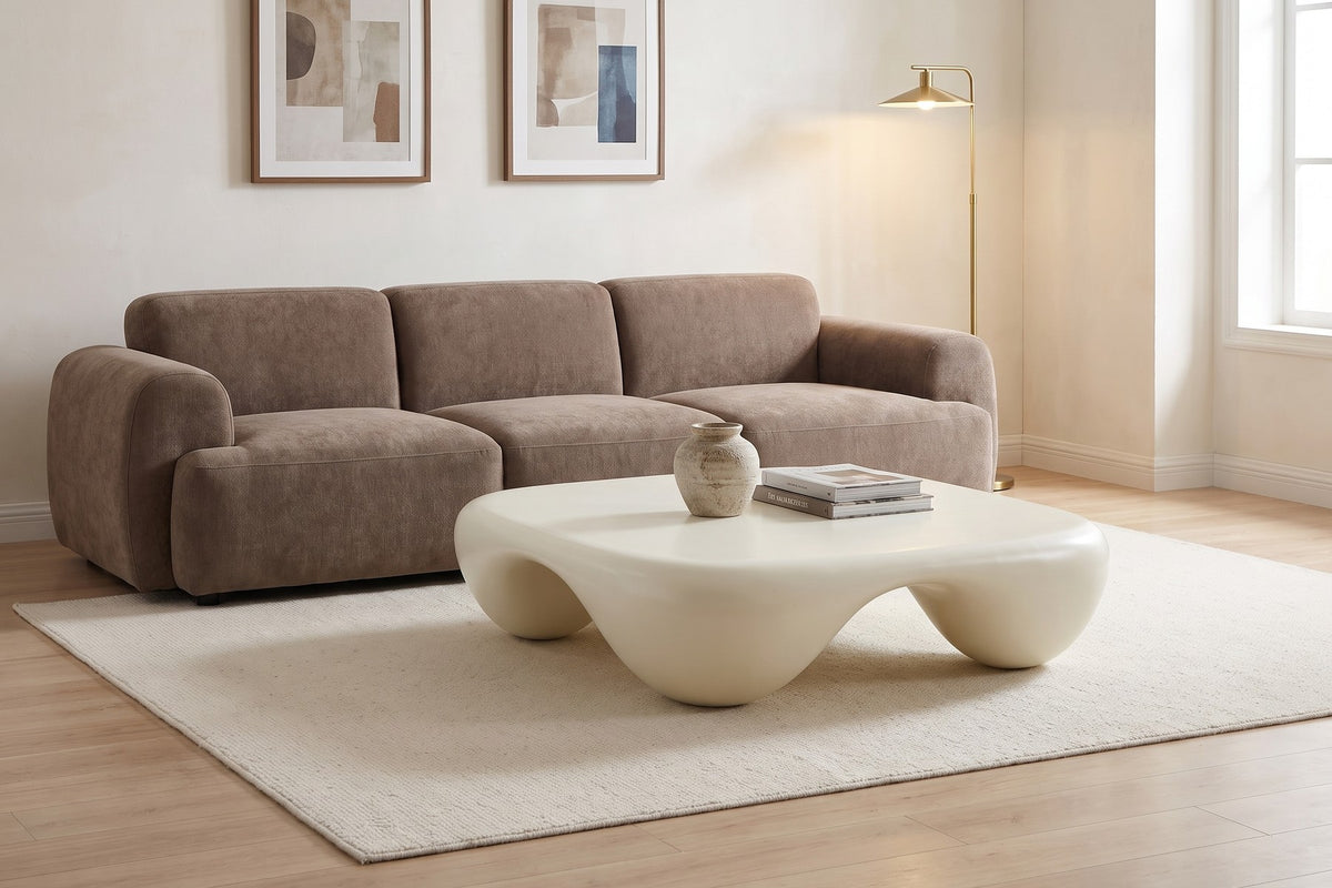 Against warm white walls and framed prints, the low, rounded square keeps the room calm.
