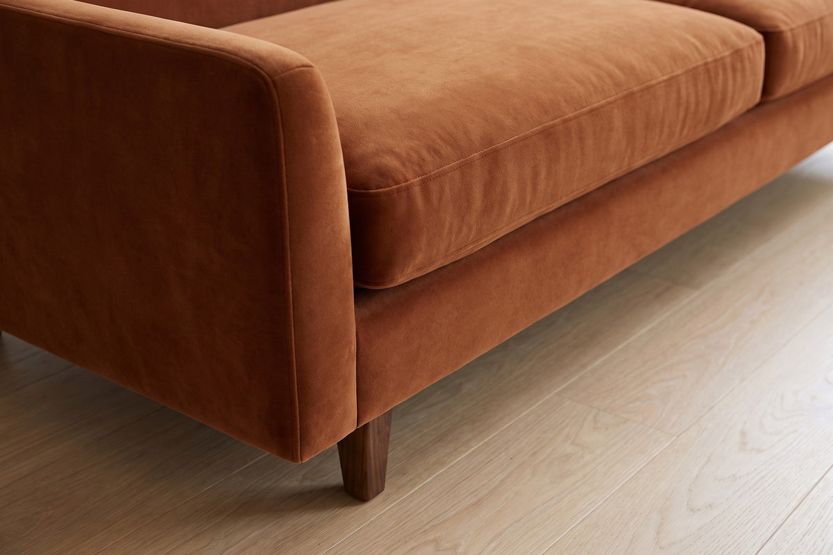 Antibes Cognac Velvet Sofa: close-up of a slim rounded arm and a short tapered walnut-finish leg below it, on a pale oak floor
