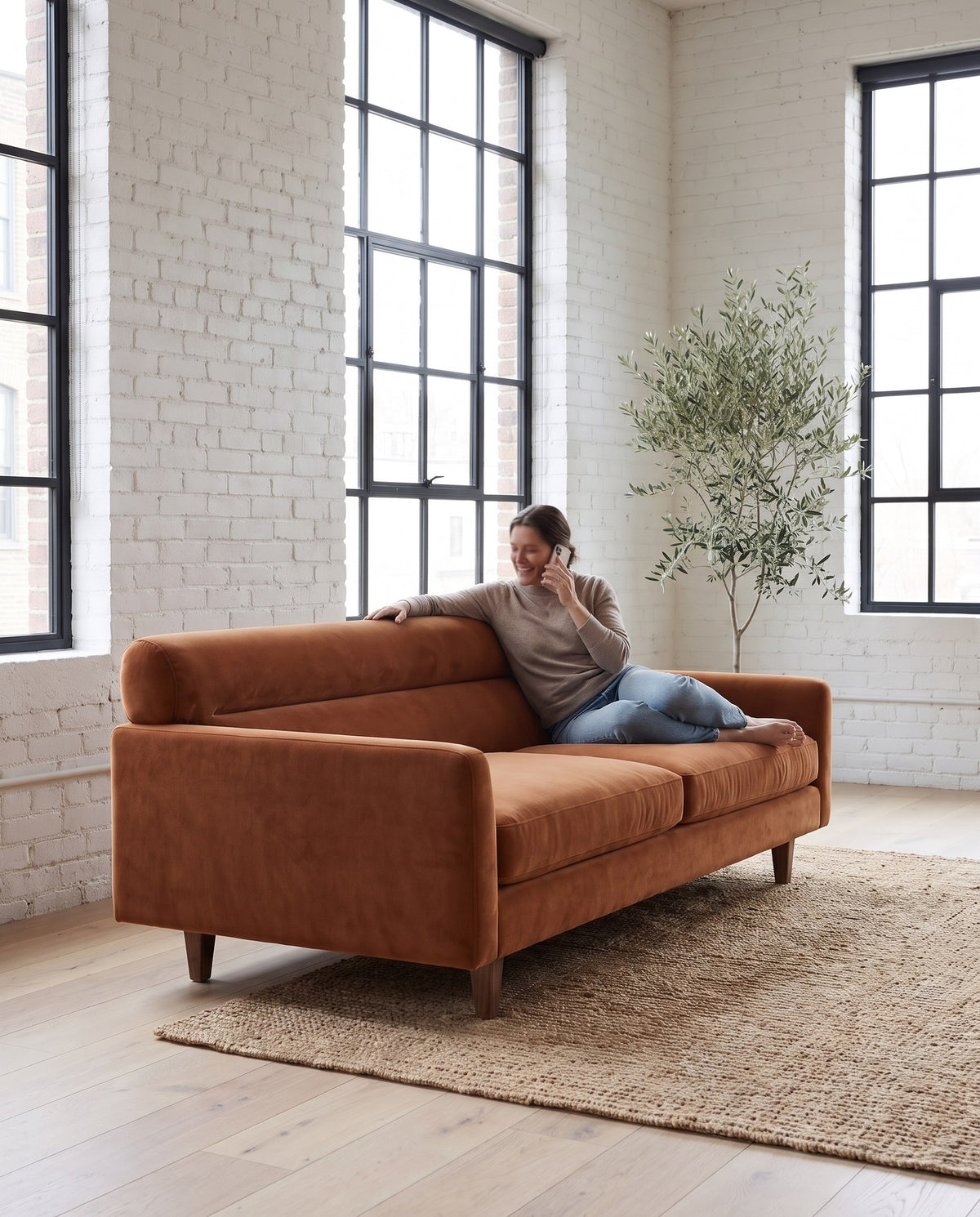A person relaxing along the Antibes cognac velvet sofa, arm resting on its rolled back (concept image)