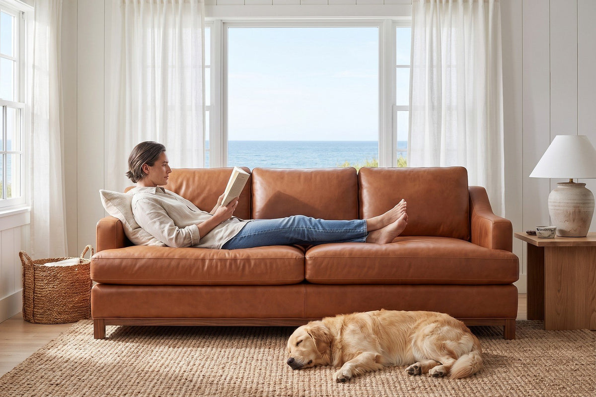 Arcachon Cognac Deep Leather Sofa in a coastal cottage, a woman reading stretched out and a dog asleep on the rug