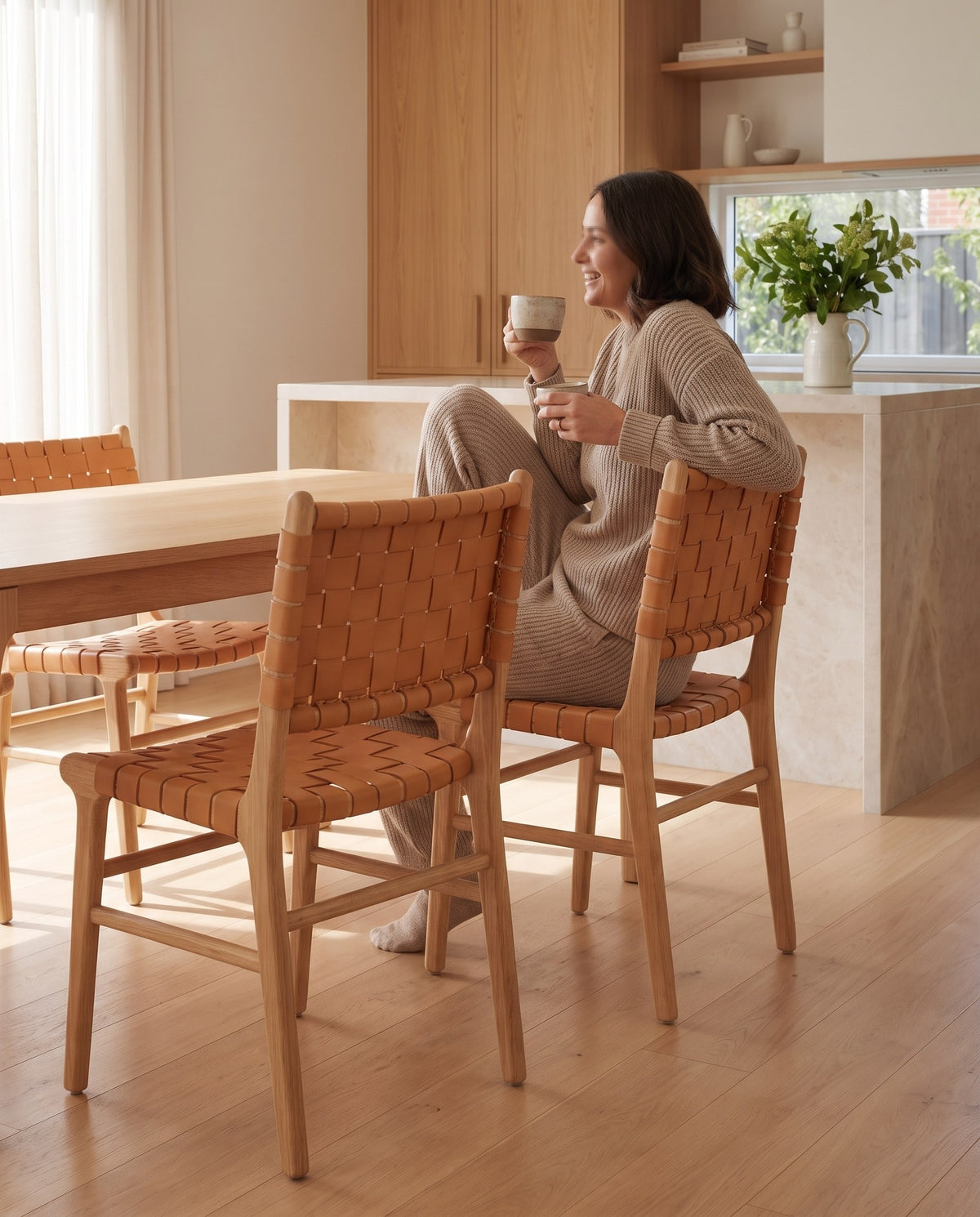 A person with a coffee sitting on an Arles woven leather dining chair at an oak table (concept image)
