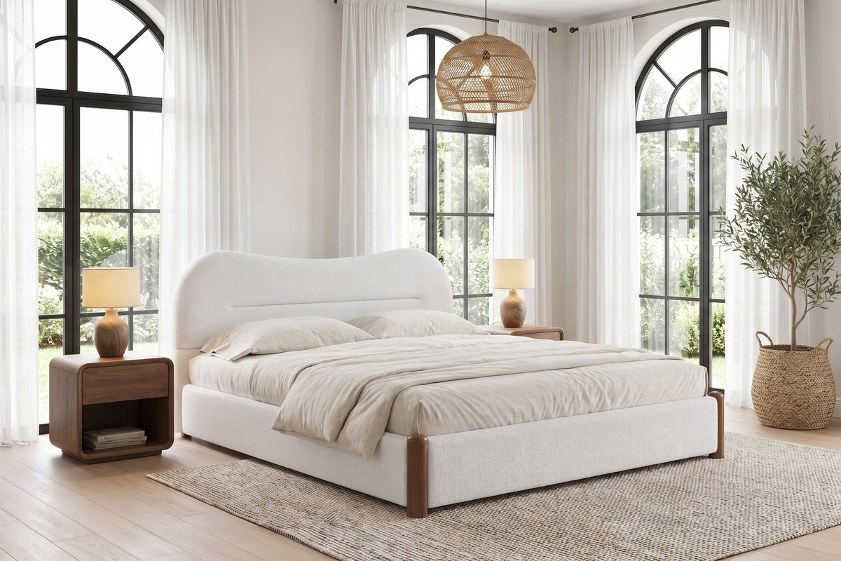 Daylight. Under tall arched windows, the headboard rises in its soft wave.