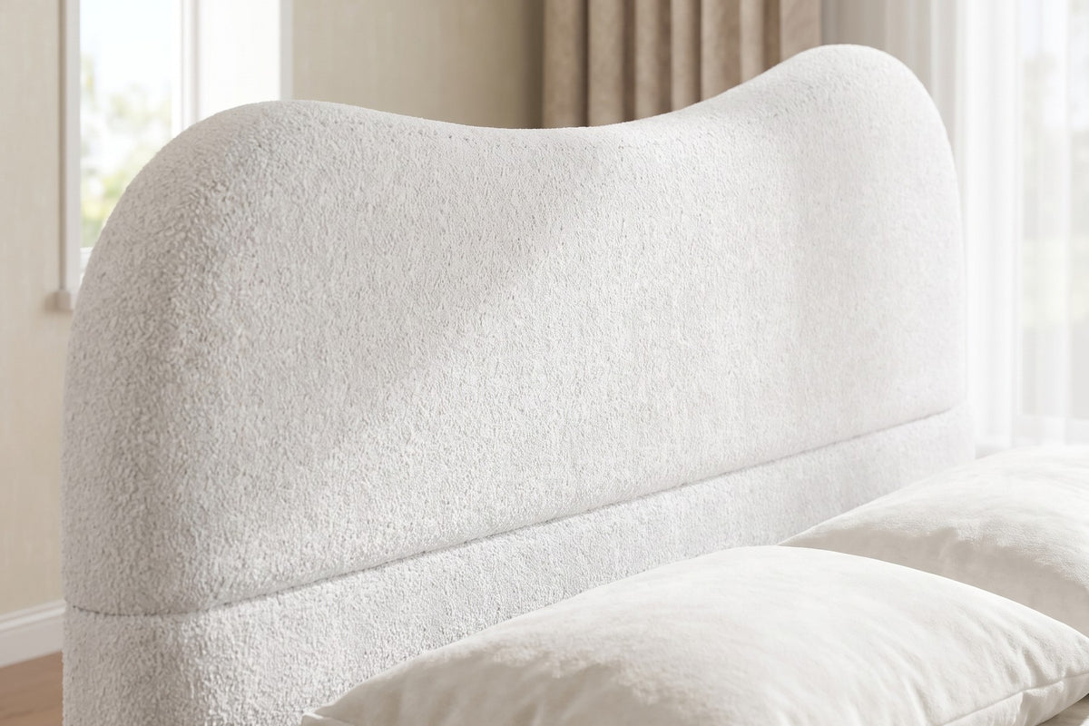 Close-up of the headboard's wavy, rounded top in soft white Berber fleece, seen slightly from one side, with the edge of a white pillow (Aurore)