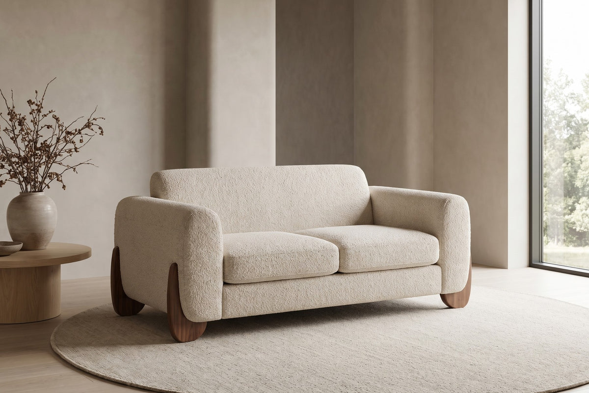 Auteuil almond bouclé loveseat with sculpted walnut-finish feet in a calm, daylit living room