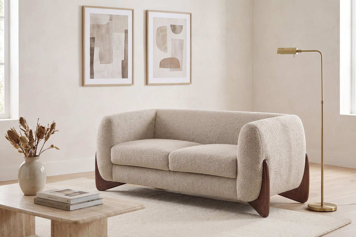 Auteuil almond bouclé loveseat with sculpted walnut-finish feet in a calm living room with framed prints