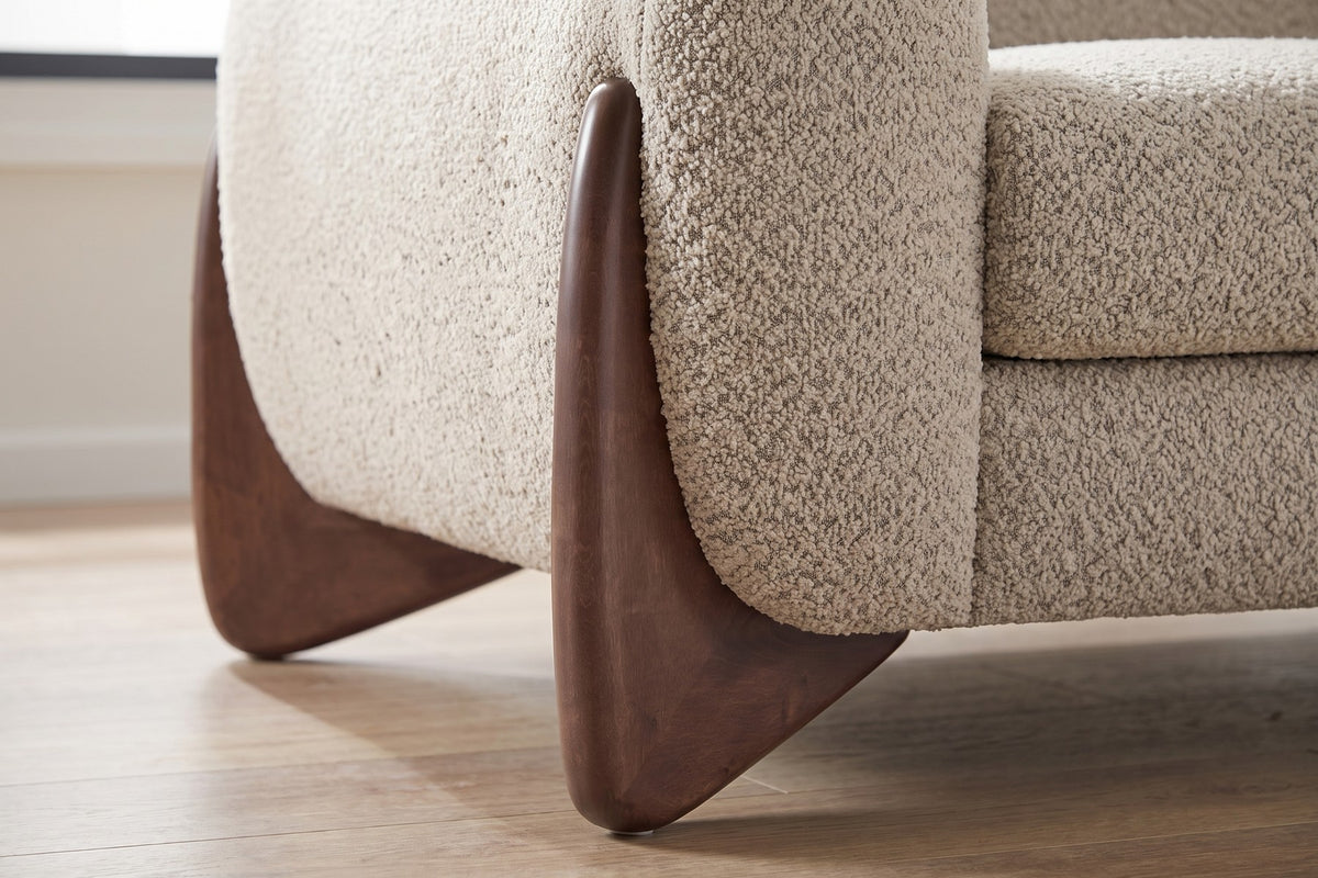 Close-up of one sculpted walnut-finish wedge foot against the boucle arm (Auteuil)