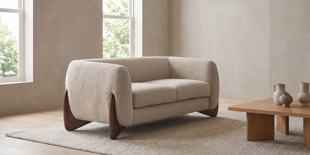 Auteuil almond bouclé loveseat with sculpted walnut-finish feet in a wide, calm living room