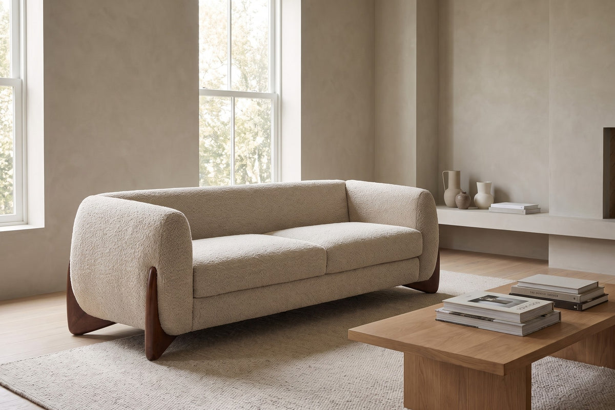 Auteuil almond bouclé sofa with sculpted walnut-finish feet in a wide, calm living room