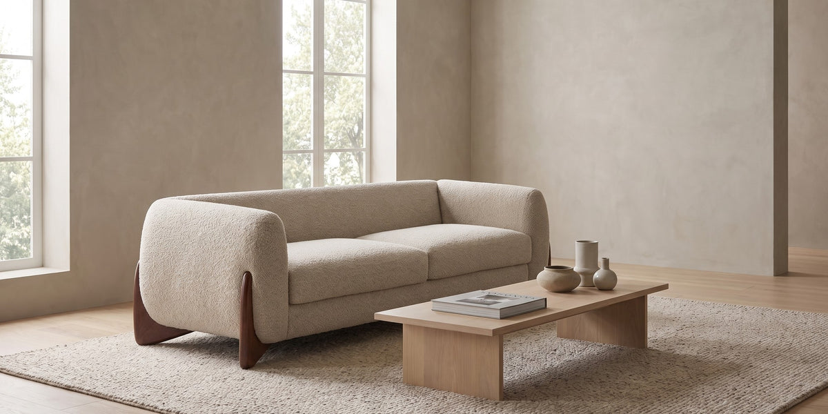 Auteuil almond bouclé sofa with sculpted walnut-finish feet in a wide, calm living room