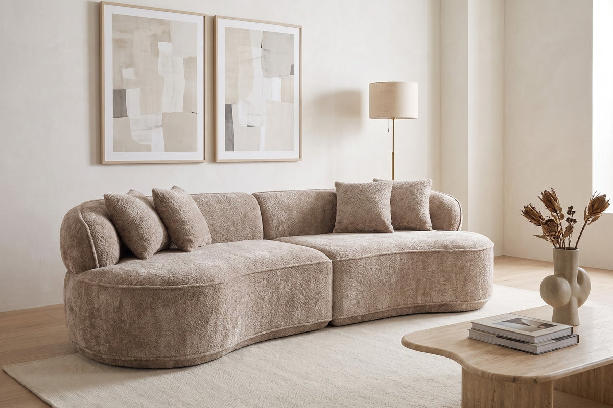 Daytime. Under two large prints, a curved coffee table follows the sofa's soft line.