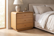 Belleville natural-finish 3-drawer nightstand with curved edges beside a bed in a calm bedroom