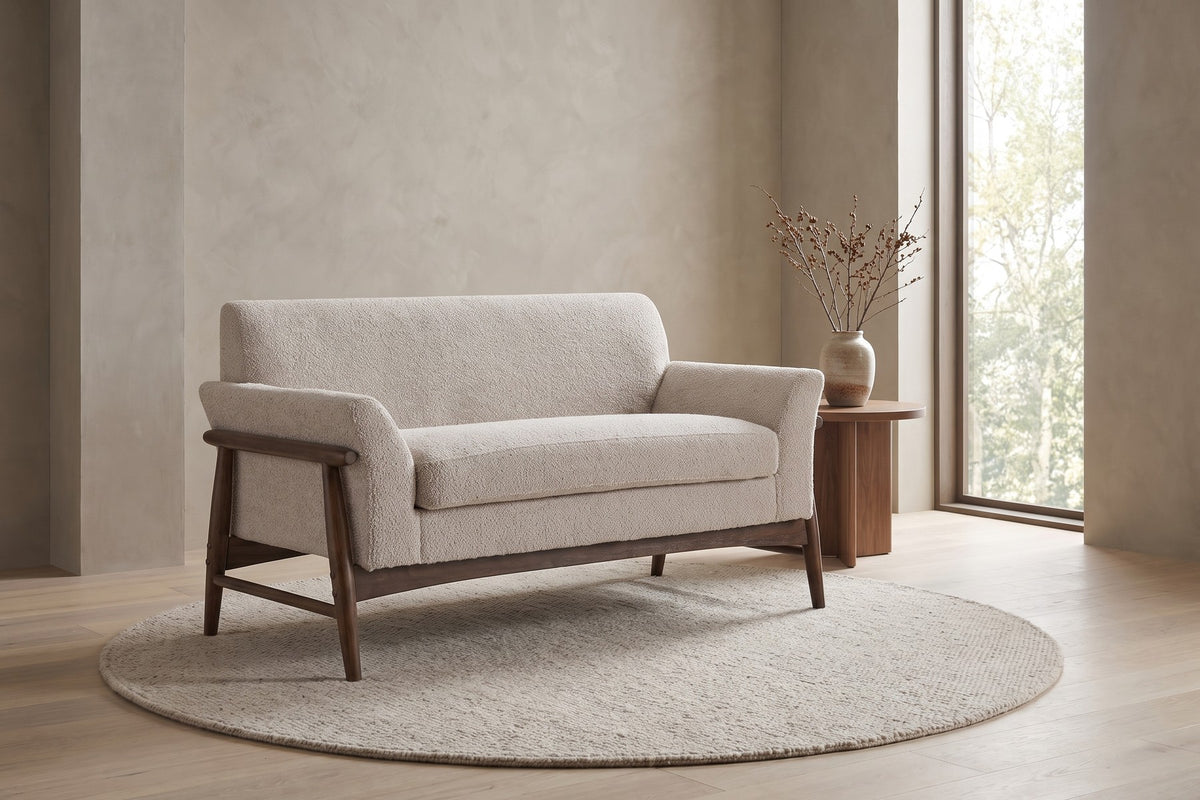 Bercy almond bouclé loveseat with flared arms and a walnut-finish frame in a calm, daylit living room