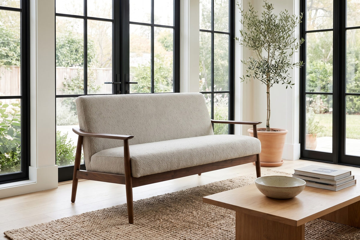 Bercy almond bouclé loveseat with flared arms and a walnut-finish frame in a bright sunroom-style living room