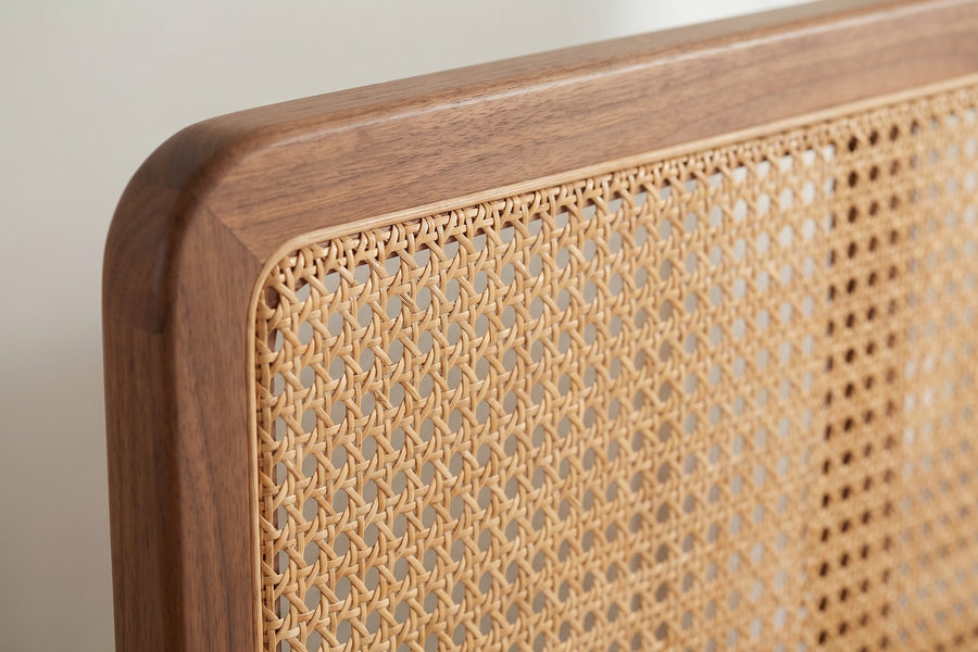 Bergerac Walnut and Cane Bed: close-up of the hand-woven natural cane panel where it meets the rounded top corner of the walnut headboard frame, showing the weave and the grain