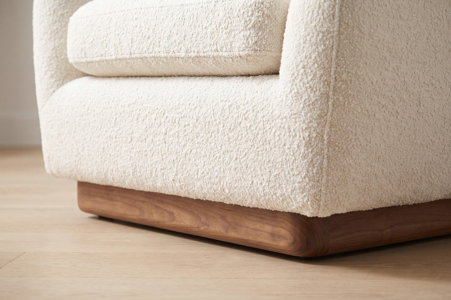 Biot Ivory Bouclé Lounge Chair: close-up of the low solid walnut plinth under the front edge of the chair, its rounded edge and grain, on a pale oak floor