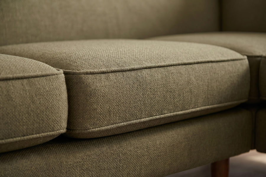Cabourg Olive Corner Sectional: close-up of the tight back's horizontal seam above the welted edge of a seat cushion, the olive woven texture visible