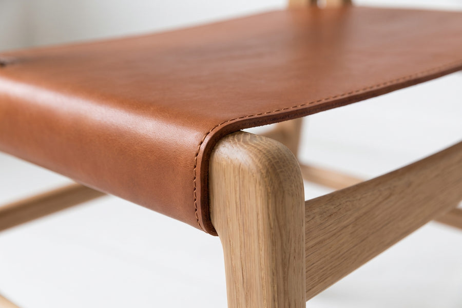 Cassis Leather Sling Dining Chair: close-up of where the cognac leather seat sling wraps around the front oak seat rail, showing the stitched edge and the leather grain