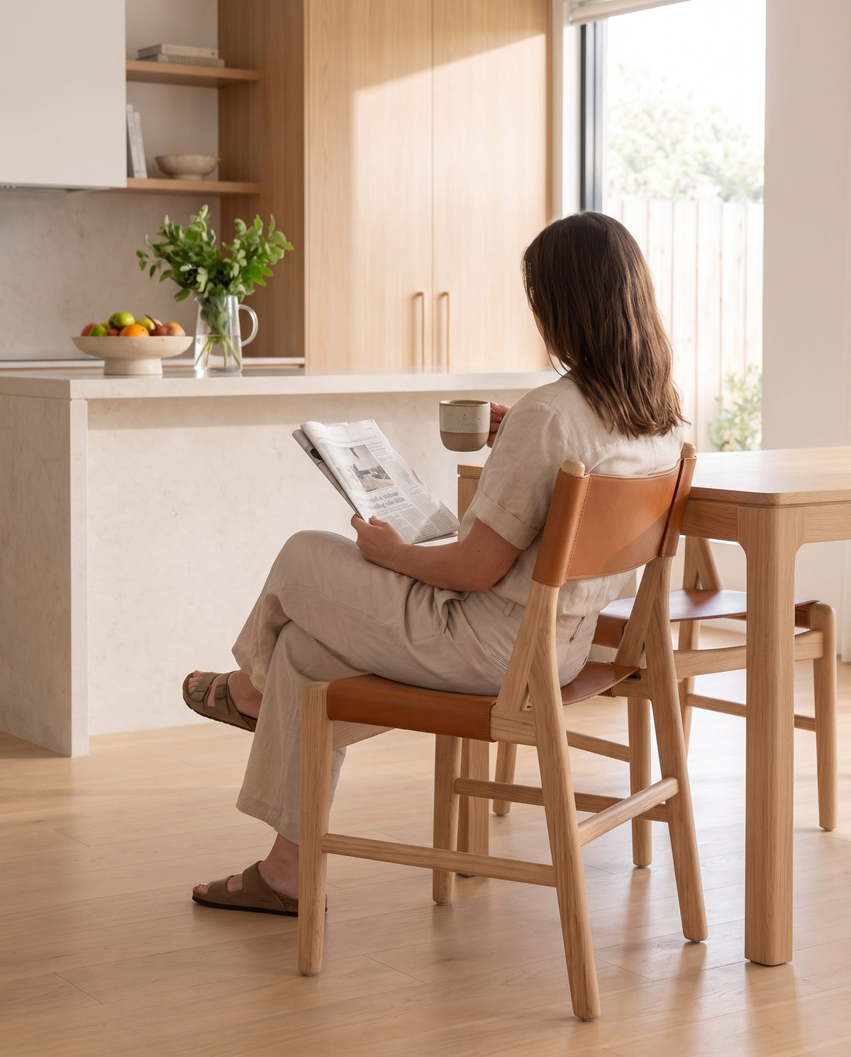 A person reading the paper on a Cassis leather sling dining chair (concept image)