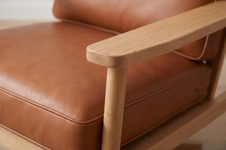Chinon Cognac Leather and Oak Swivel Chair: close-up of the wide flat oak armrest with its softly rounded edge and the slim front oak post, beside the cognac leather seat cushion