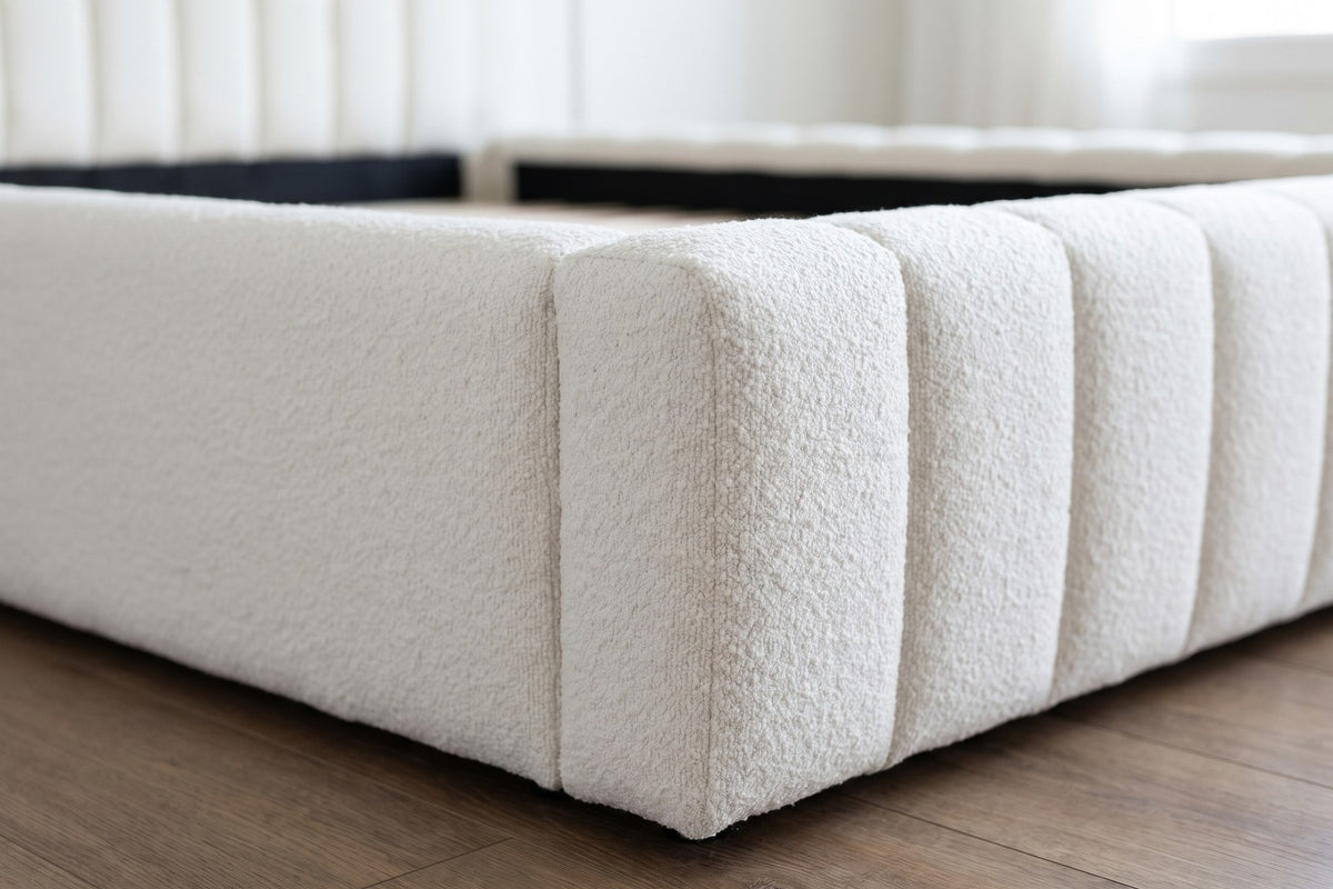 Close-up of the corner where the channel-tufted white bouclé side rail meets the foot of the bed (Clémence)