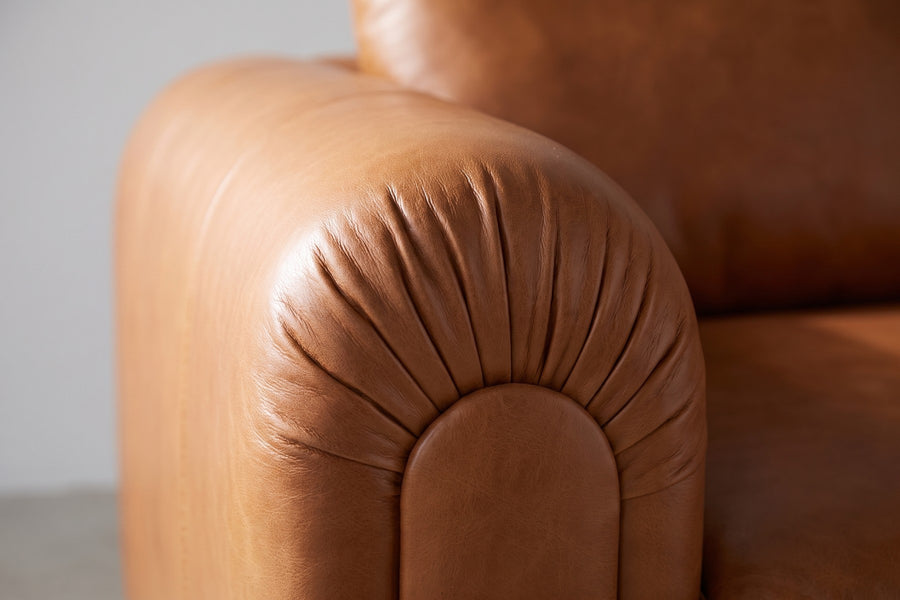 Collioure Cognac Leather Low Sofa: close-up of a rounded arm front, showing the cognac leather softly gathered into fine folds where it wraps the curve