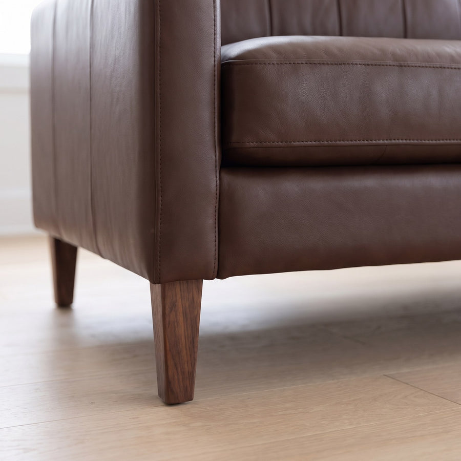 Close-up of the Colmar sofa's tapered walnut-finish leg and rounded leather arm