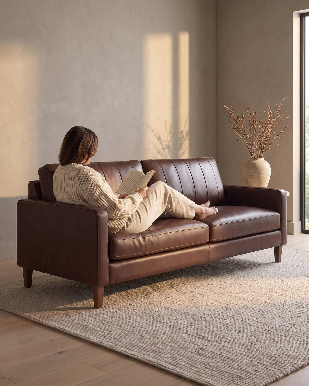 A person reading with their legs stretched out on the chocolate leather Colmar sofa