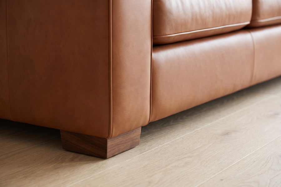 Deauville Cognac Leather Sofa: close-up of a low rectangular walnut-finish block foot under the front corner of the sofa, on a pale oak floor