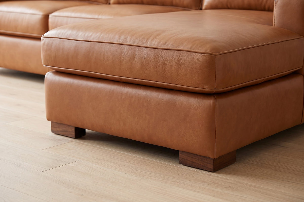 Deauville Cognac Leather Chaise Sectional: close-up of a low rectangular walnut-finish block foot under the front corner of the chaise, on a pale oak floor