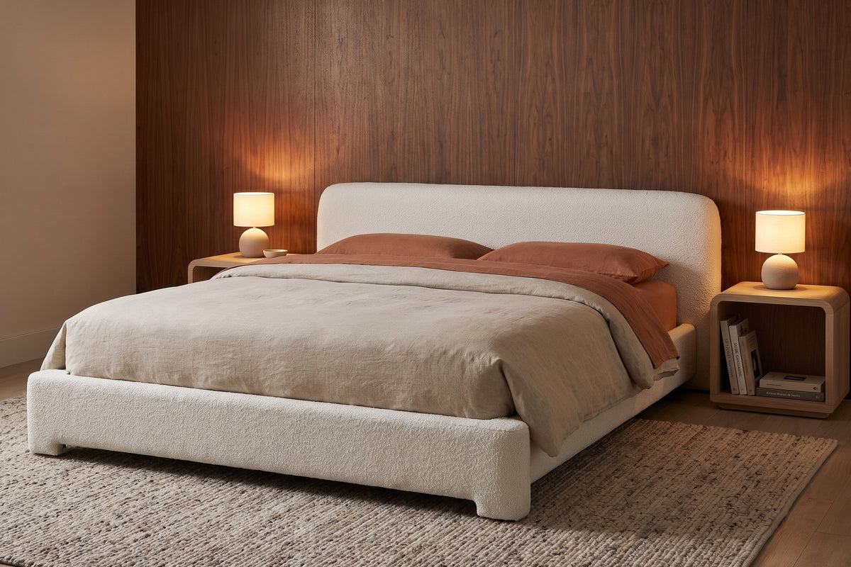Elodie low white bouclé platform bed with rounded rails in a warm walnut-panelled bedroom in the evening