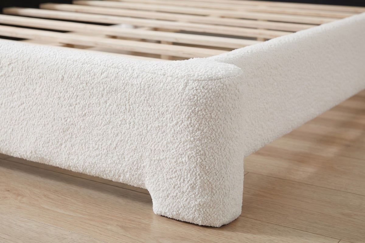 Close-up of one foot corner where the rounded white bouclé rail turns down into a short upholstered block foot (Elodie)