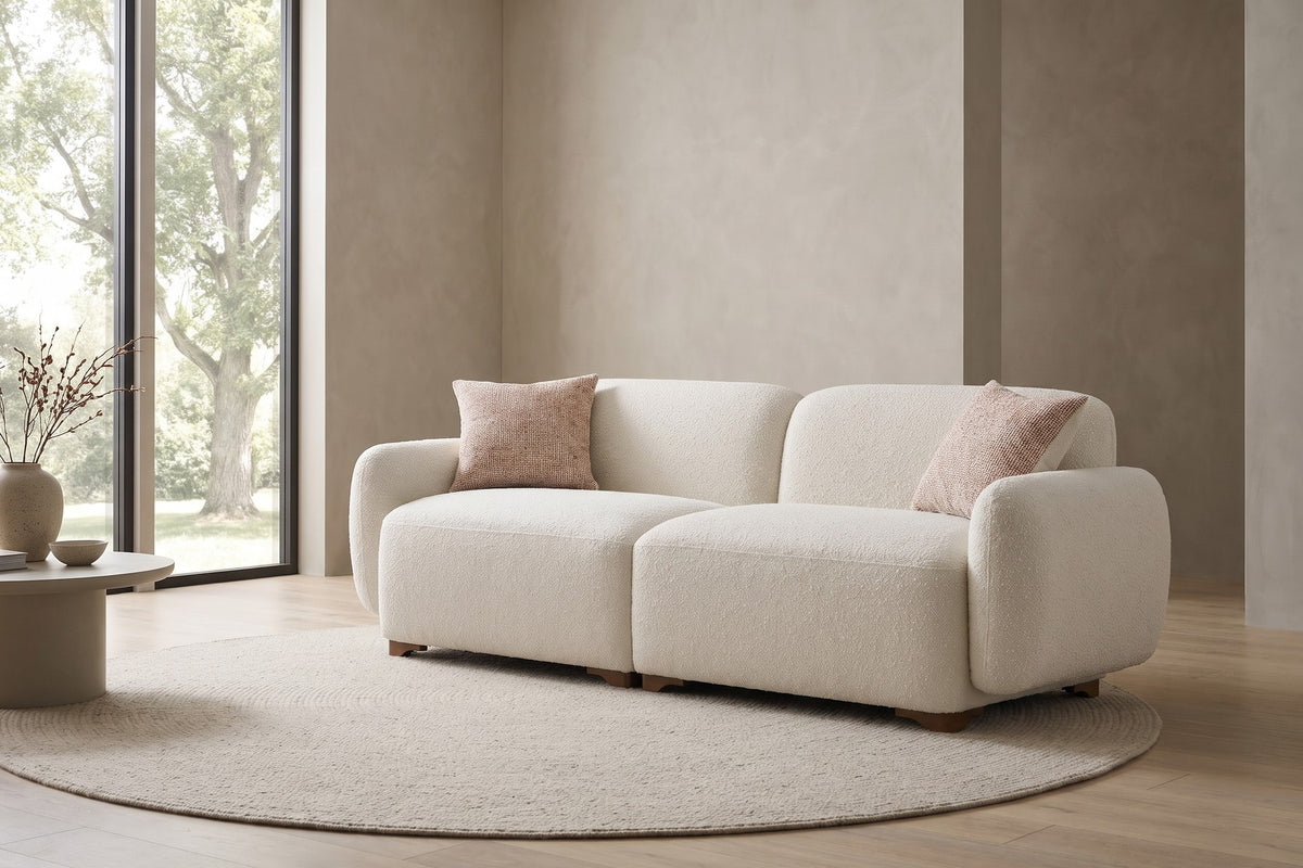 In a calm, daylit room, the cream bouclé and rounded arms keep the shape soft.