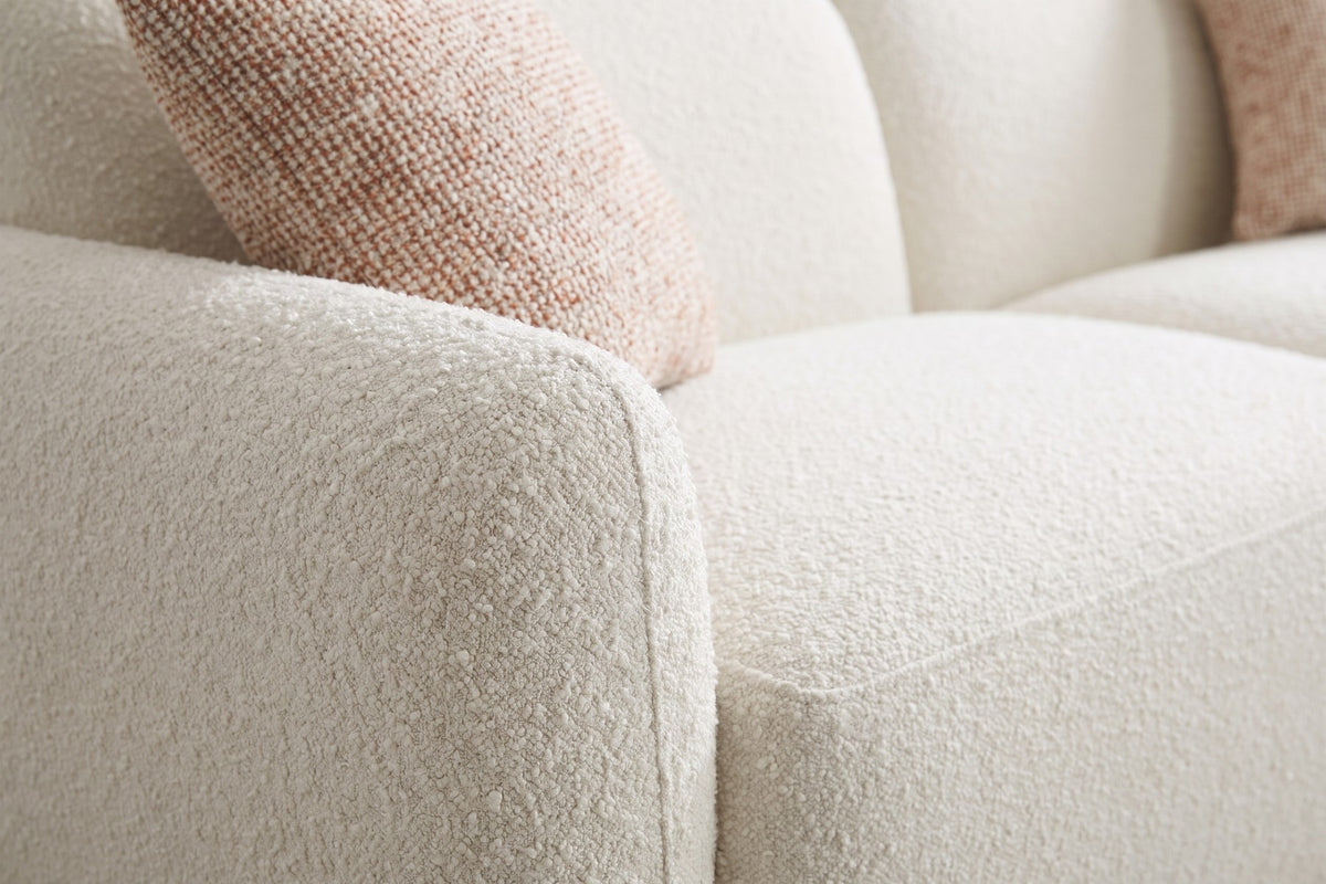 Close-up of the cream bouclé texture on the rounded arm, with one flecked pillow beside it (Estelle)