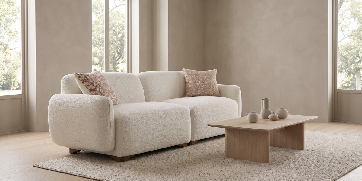 Estelle cream bouclé rounded sofa with two flecked pillows in a wide room view