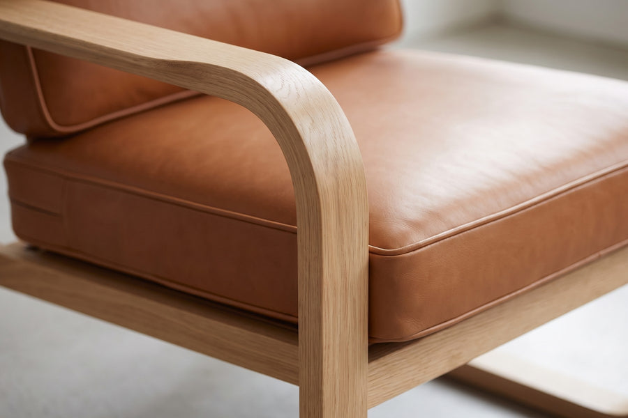 Étretat Bentwood Oak and Cognac Leather Lounge Chair: close-up of the oak side loop where the armrest bends down into the front leg, showing the smooth curve and the oak grain, beside the cognac seat cushion