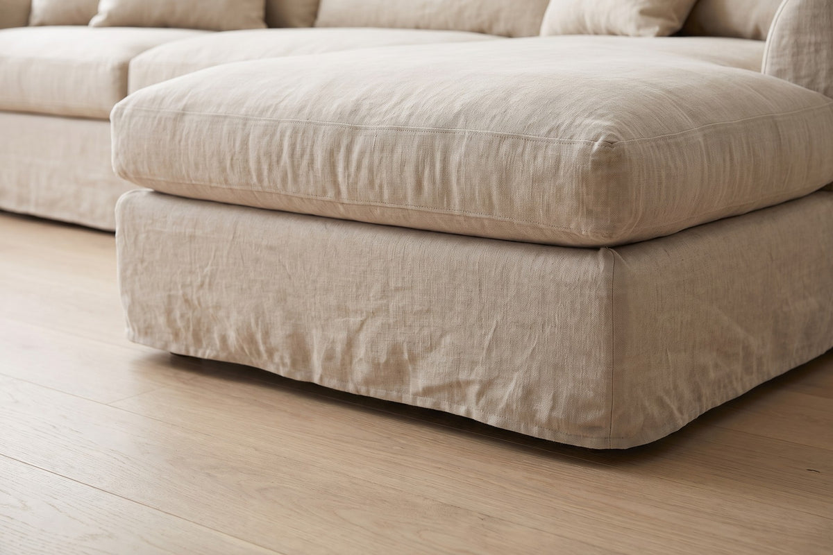 Germain Natural Linen Slipcovered Chaise Sectional: close-up of the short tailored skirt at the front corner of the chaise, just above a pale oak floor