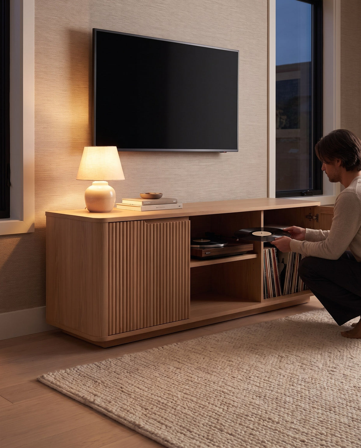 A person putting a record on the turntable in the open bay of the Gordes fluted oak console (concept image)