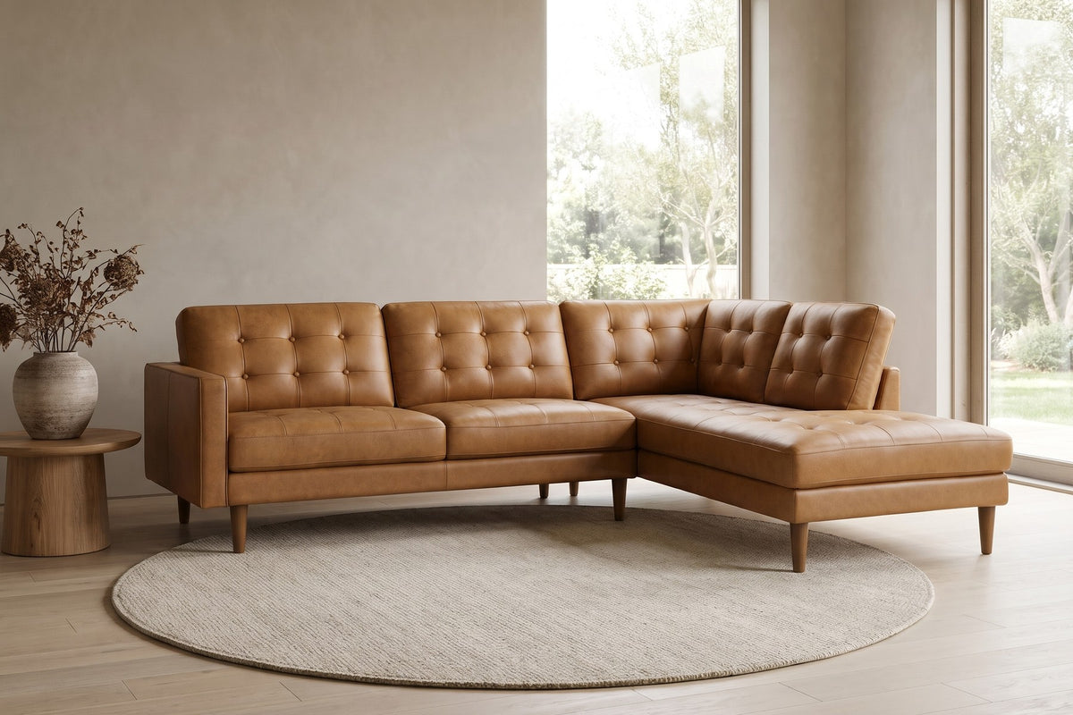 In a calm, daylit room, the tan leather and tufted back sit on slim tapered legs.