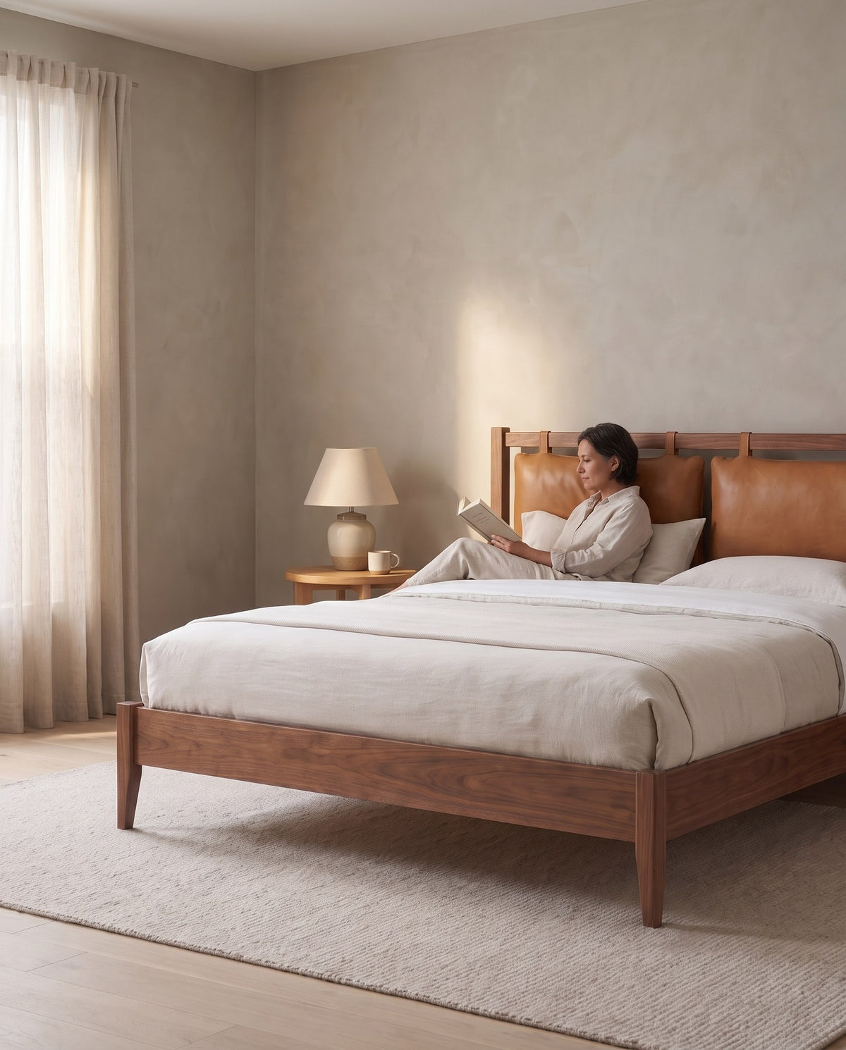 A person reading in the Honfleur walnut bed, leaning on the leather headboard cushions (concept image)