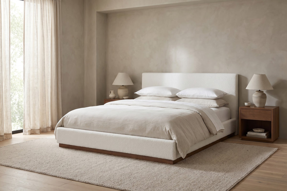 Jeanne white upholstered bed with a brown rubberwood base in a calm, daylit bedroom