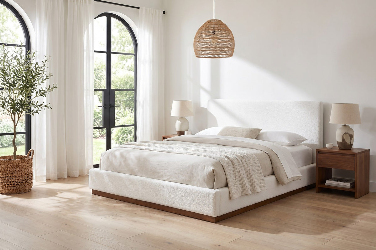 Jeanne white upholstered bed with a brown rubberwood base in a bright bedroom with tall arched windows