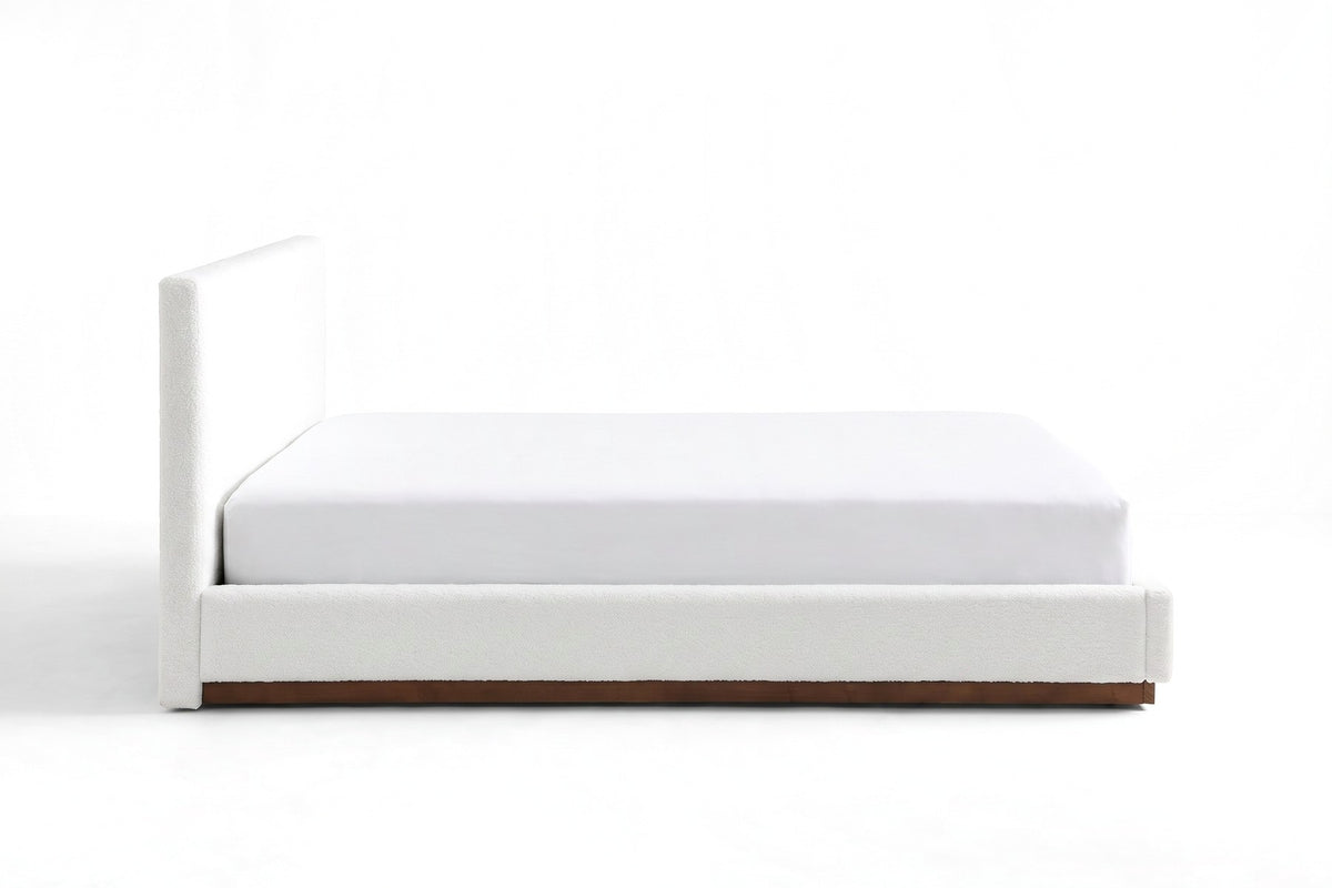Jeanne white upholstered bed with a brown rubberwood base, straight side view at mattress height on a white background
