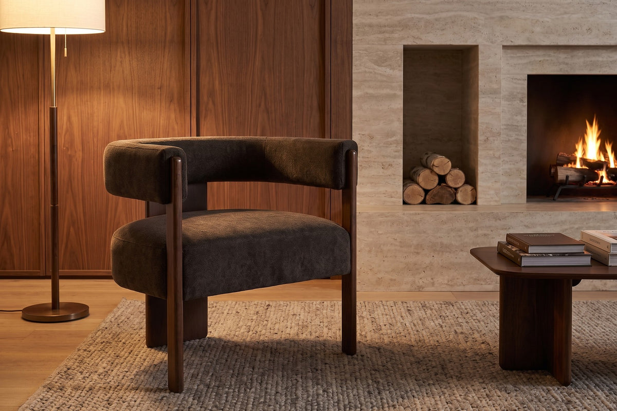 Juliette dark brown velvet barrel accent chair with a walnut-finish frame in a warm walnut-panelled living room in the evening