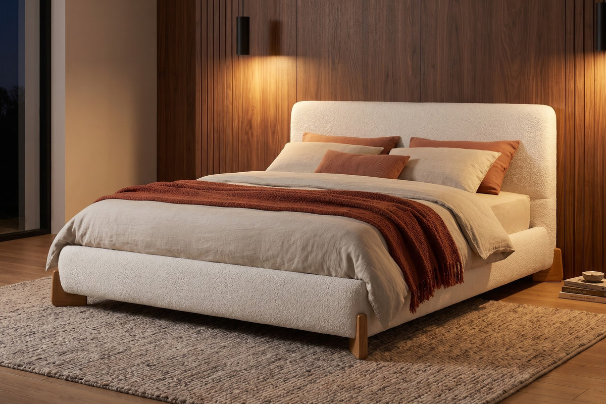 Léonie white bouclé king platform bed with natural wood corner feet in a warm walnut-panelled bedroom in the evening