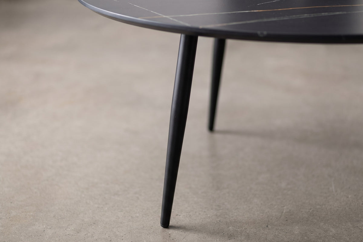 Close-up of one slim black leg of the Marais table tapering to the floor