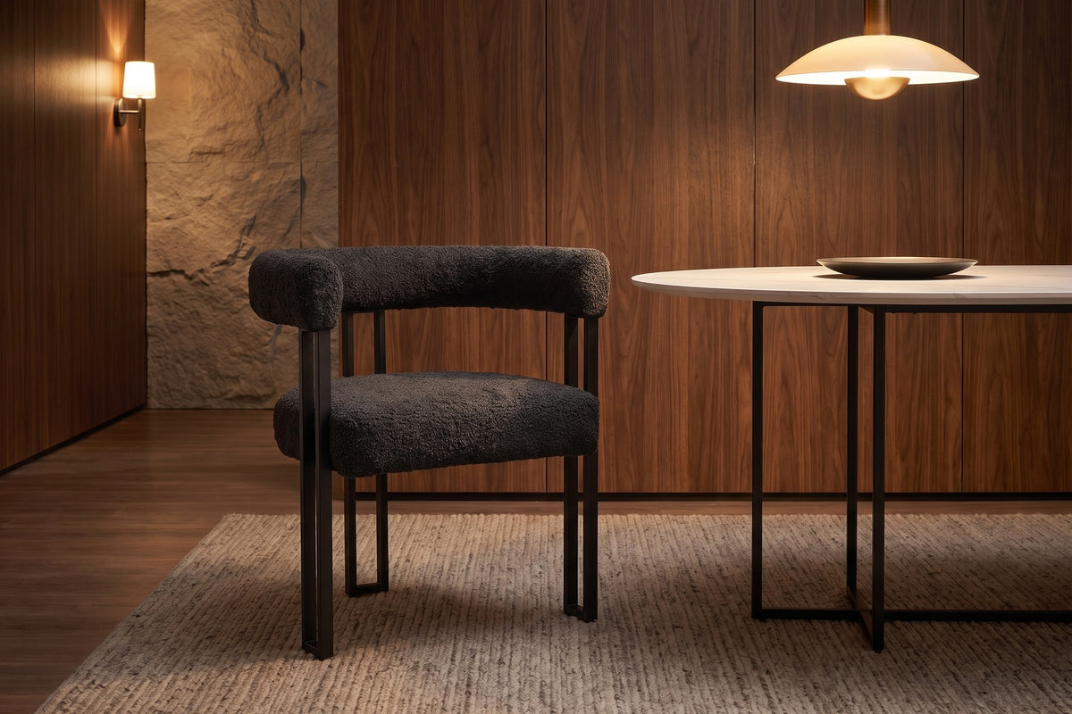 Mathilde black bouclé barrel dining armchair with black metal legs in a warm walnut-panelled dining room in the evening