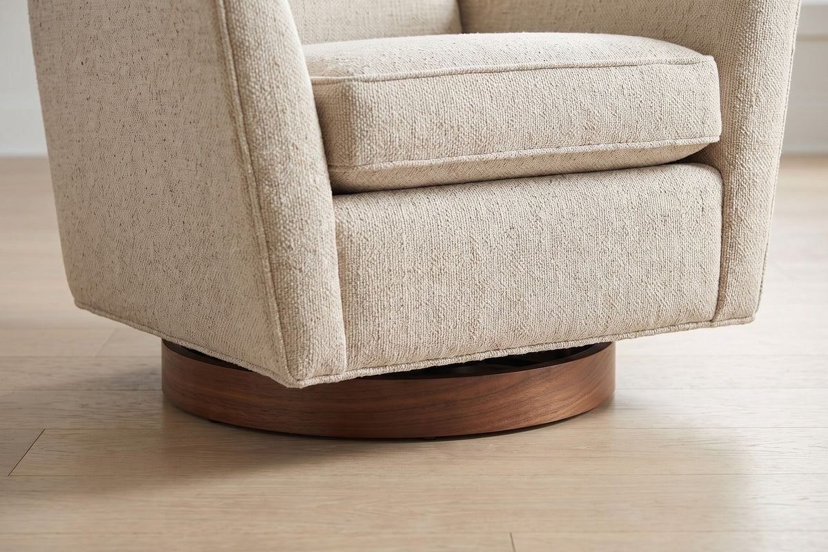 Megève Oatmeal Swivel Rocker Chair: close-up of the round walnut disc base under the seat cushion's front edge, on a pale oak floor